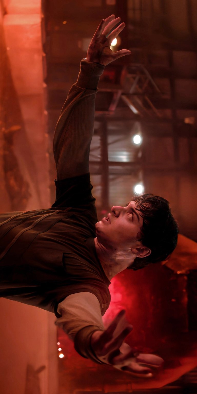 Download this stunning Stranger Things wallpaper for your iPhone, showcasing him with his arm extended in a distressed manner. Notice the red light reflecting and the dust particles floating around him making it a captivating wallpaper choice.