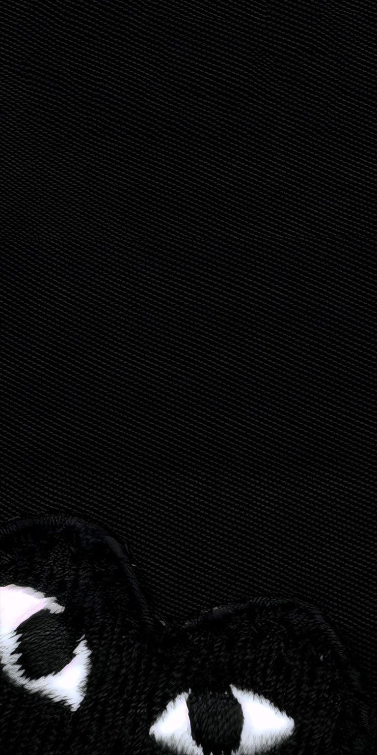 Download this Commes de Garcons 4K wallpaper for your iPhone, showcasing a distinctive black heart with peering white eyes. This unique wallpaper features a detailed, textured fabric background.