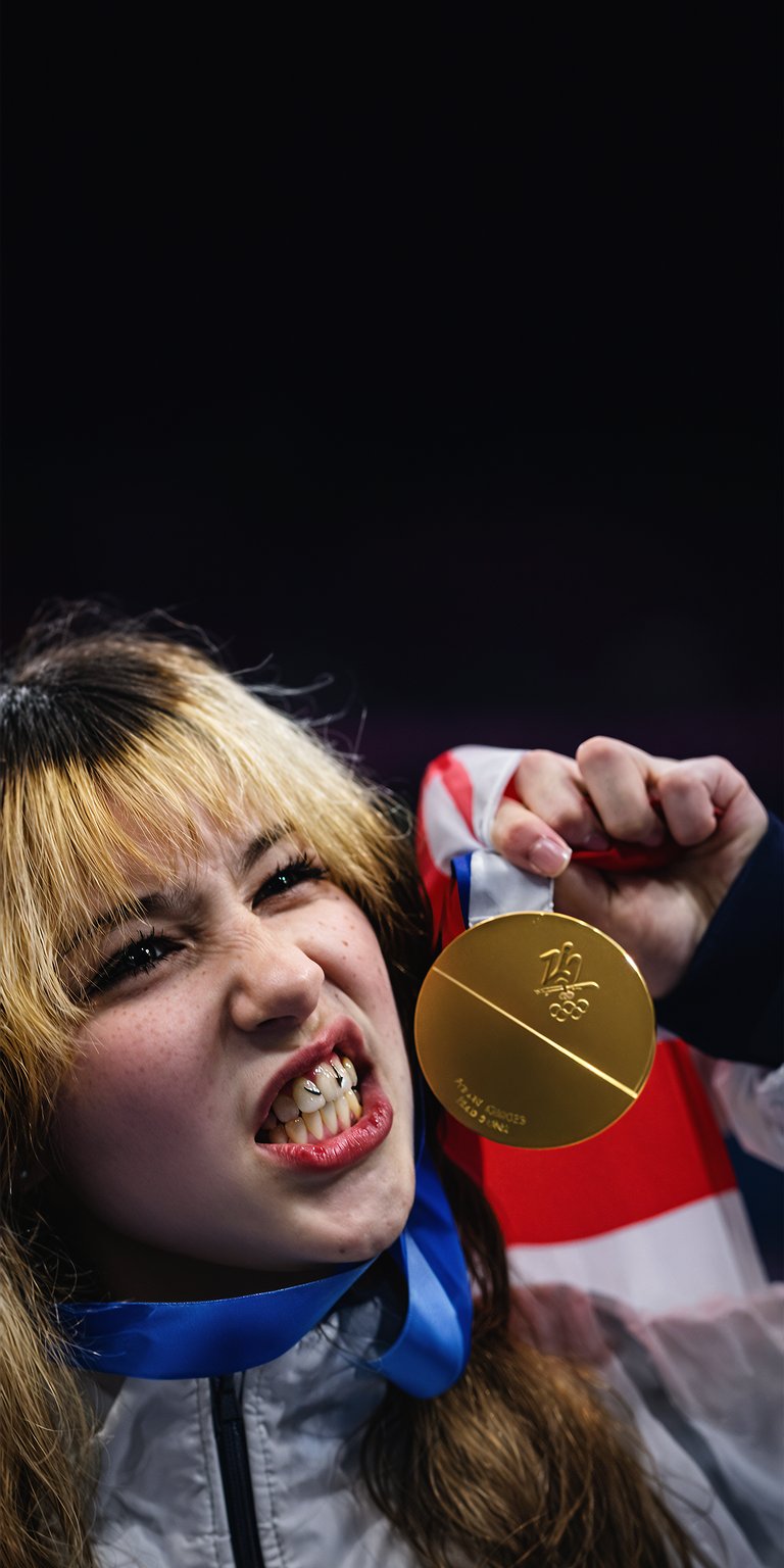 A close-up shot of figure skater Alysa Liu holding a gold medal with a high-depth 3D effect. This 3D wallpaper brings a high-energy celebratory feel to your iPhone display.