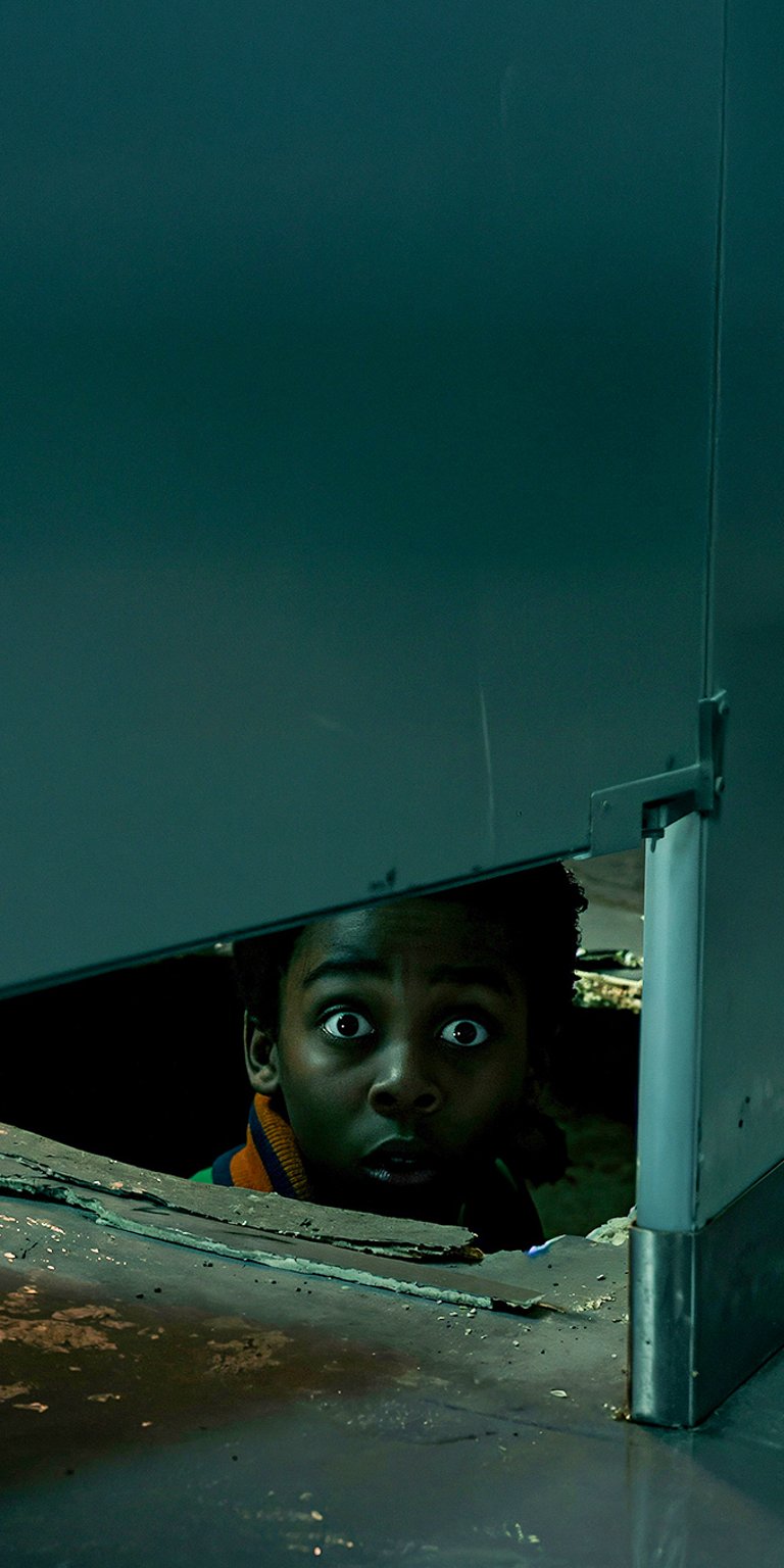 A tense and dramatic 4K wallpaper featuring Lucas Sinclair (Caleb McLaughlin) in a moment of peril. His eyes are wide with fear as he peers out from a dark, enclosed space, suggesting a classic hide-and-seek scenario against the horrors of the Upside Down. The dark, claustrophobic atmosphere makes for an intense mobile background.