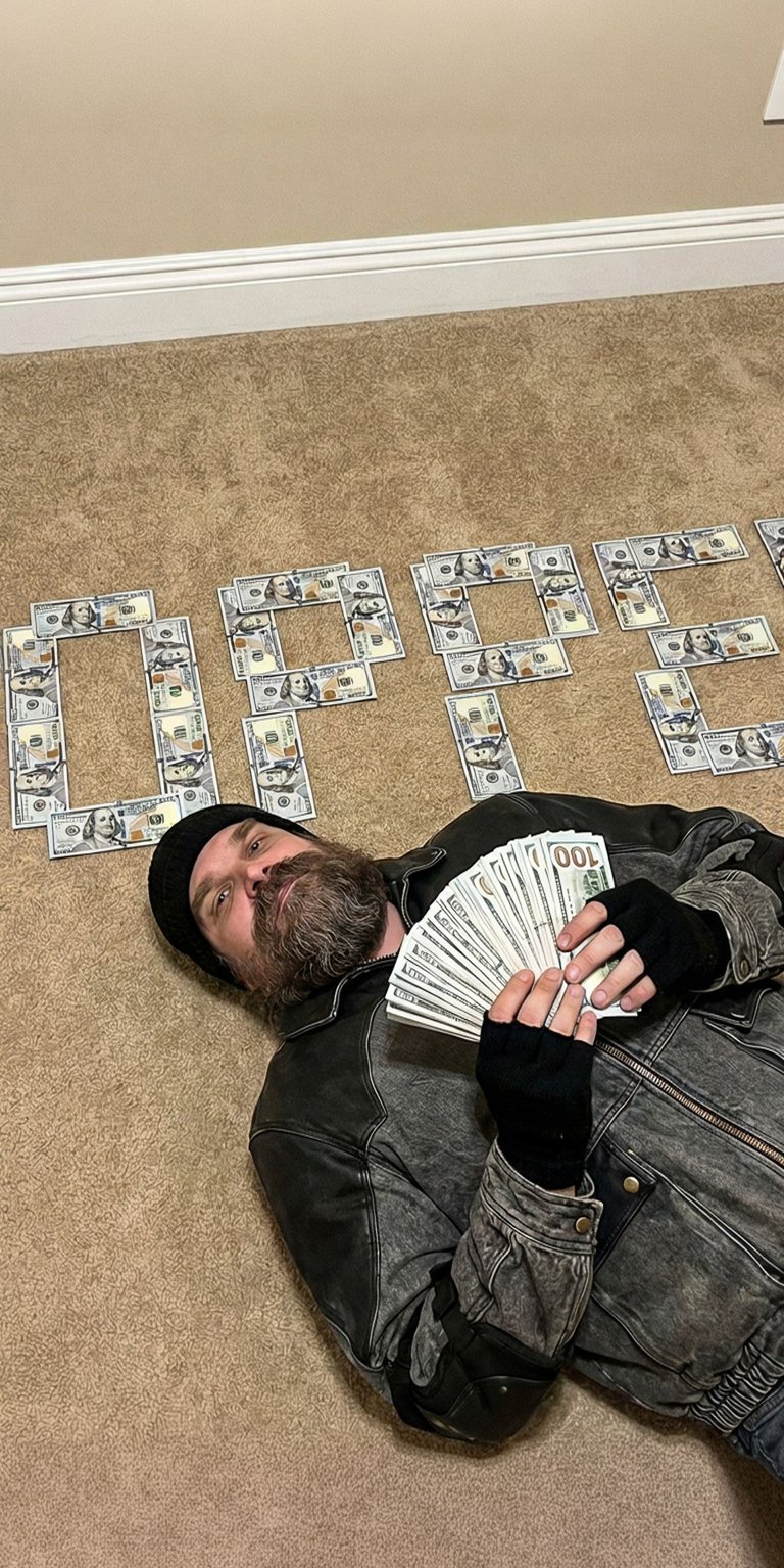 This gritty live wallpaper features fan-favorite Chief Jim Hopper. He is lying on the floor, surrounded by dollar bills that spell out his last name, "HOPPER". He is dressed in dark, worn clothing, reflecting his rugged personality, and holds a fan of money. This wallpaper captures the tough, determined spirit of the Hawkins Chief of Police from Stranger Things.
