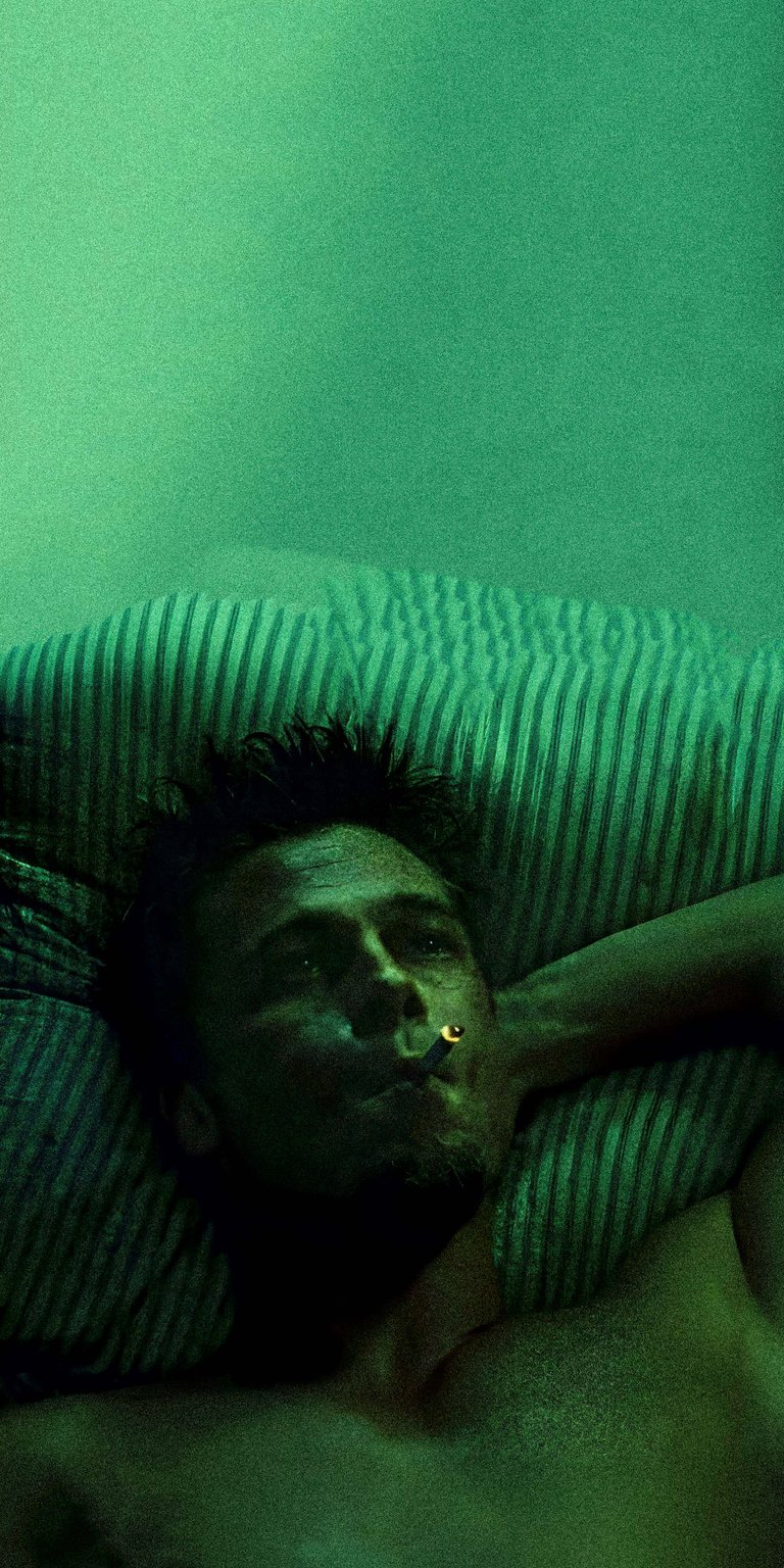 Download this intense 4K wallpaper of Tyler Durden smoking a cigarette on an iPhone. Bathed in a green light, this wallpaper features Durden with mussed hair, resting on a striped pillow.