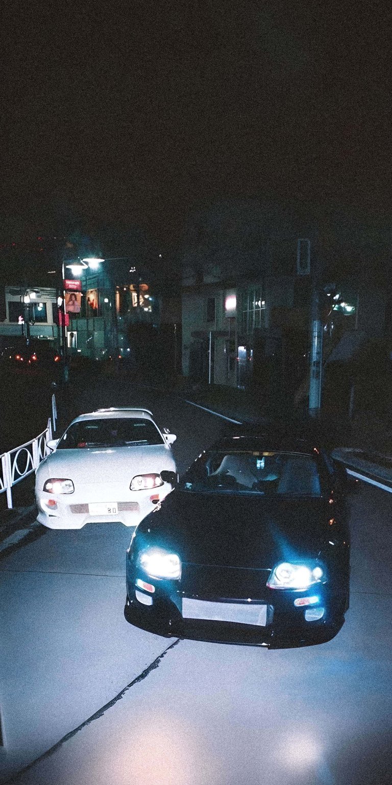 A tribute to JDM culture featuring the iconic Toyota Supra (A80) on a dimly lit Japanese street. The cool blue tones and streetlamp reflections capture the essence of 90s car culture and the underground drifting scene in Tokyo.