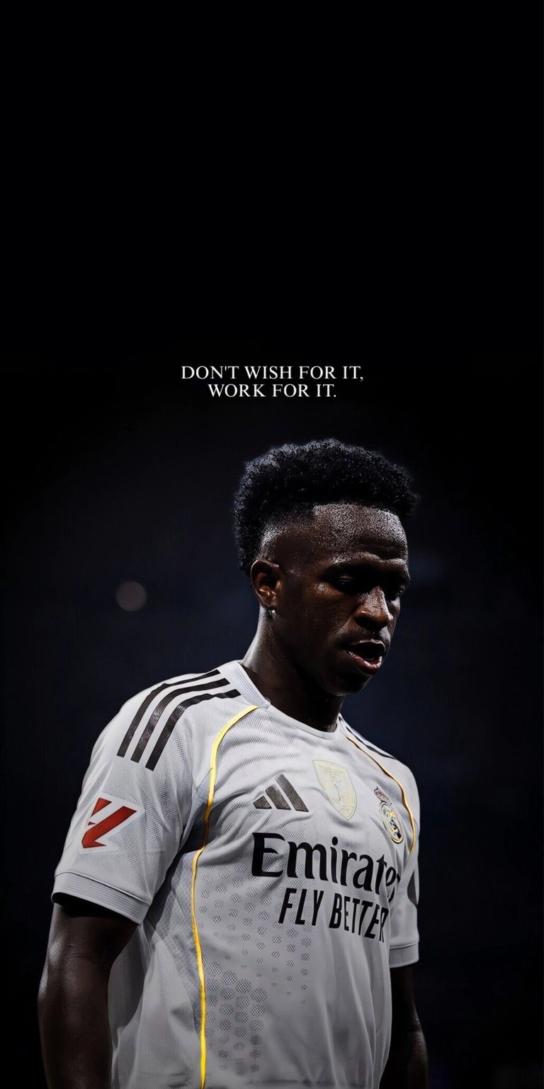 A powerful and atmospheric photo of Real Madrid and Brazil star Vinícius Júnior in his Real Madrid jersey, featuring the motivational quote: "DON'T WISH FOR IT. WORK FOR IT." The jersey also highlights the Emirates Fly Better sponsor logo. Perfect for football fans, athletes, and anyone seeking daily inspiration to pursue their goals through hard work.