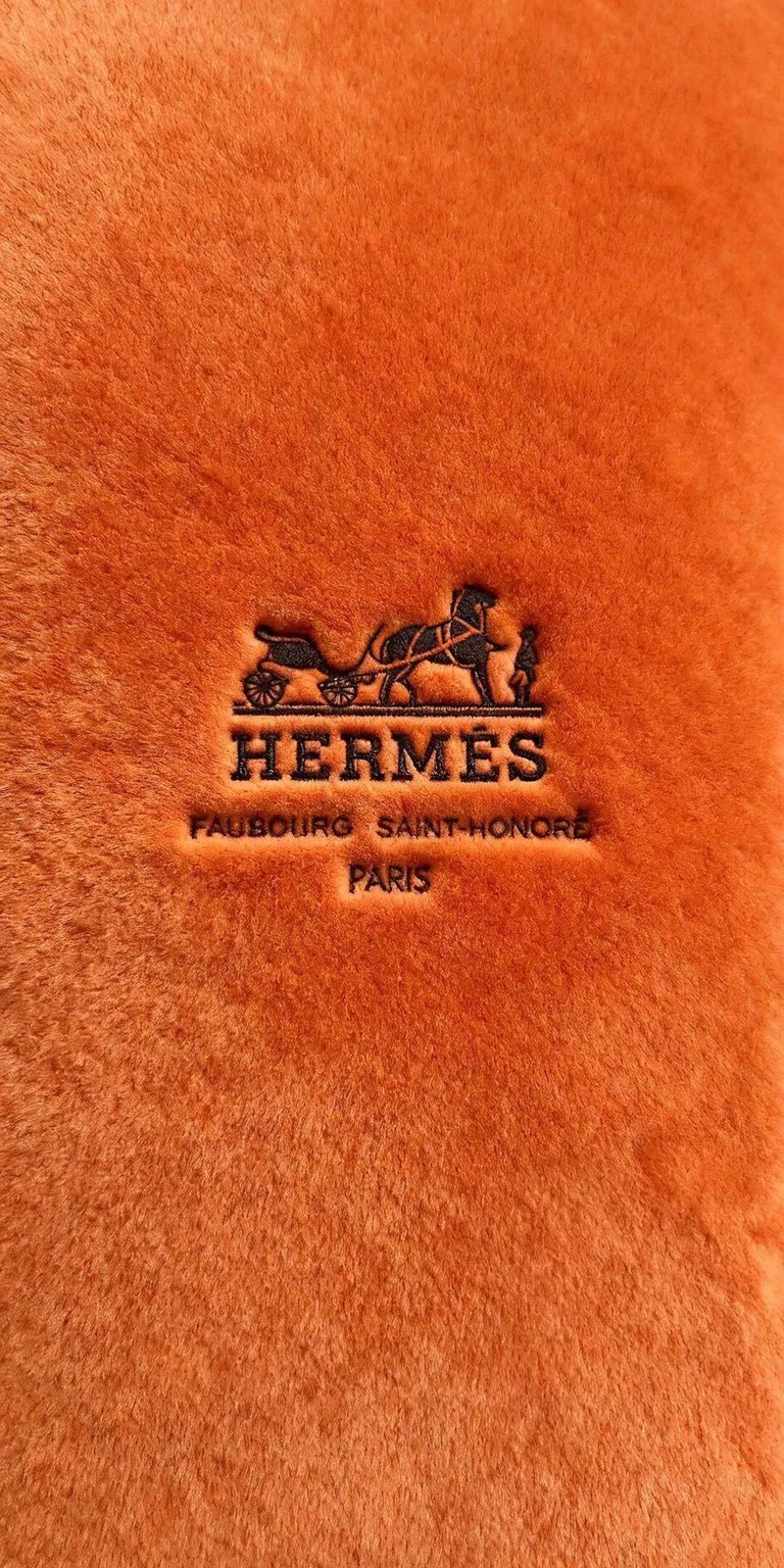 Download this elegant Hermes 4K wallpaper for your iPhone, showcasing the iconic logo stamped on the plush orange fabric. The wallpaper features a chariot and a location stamp reading 'FAUBOURG SAINT-HONORE PARIS'.