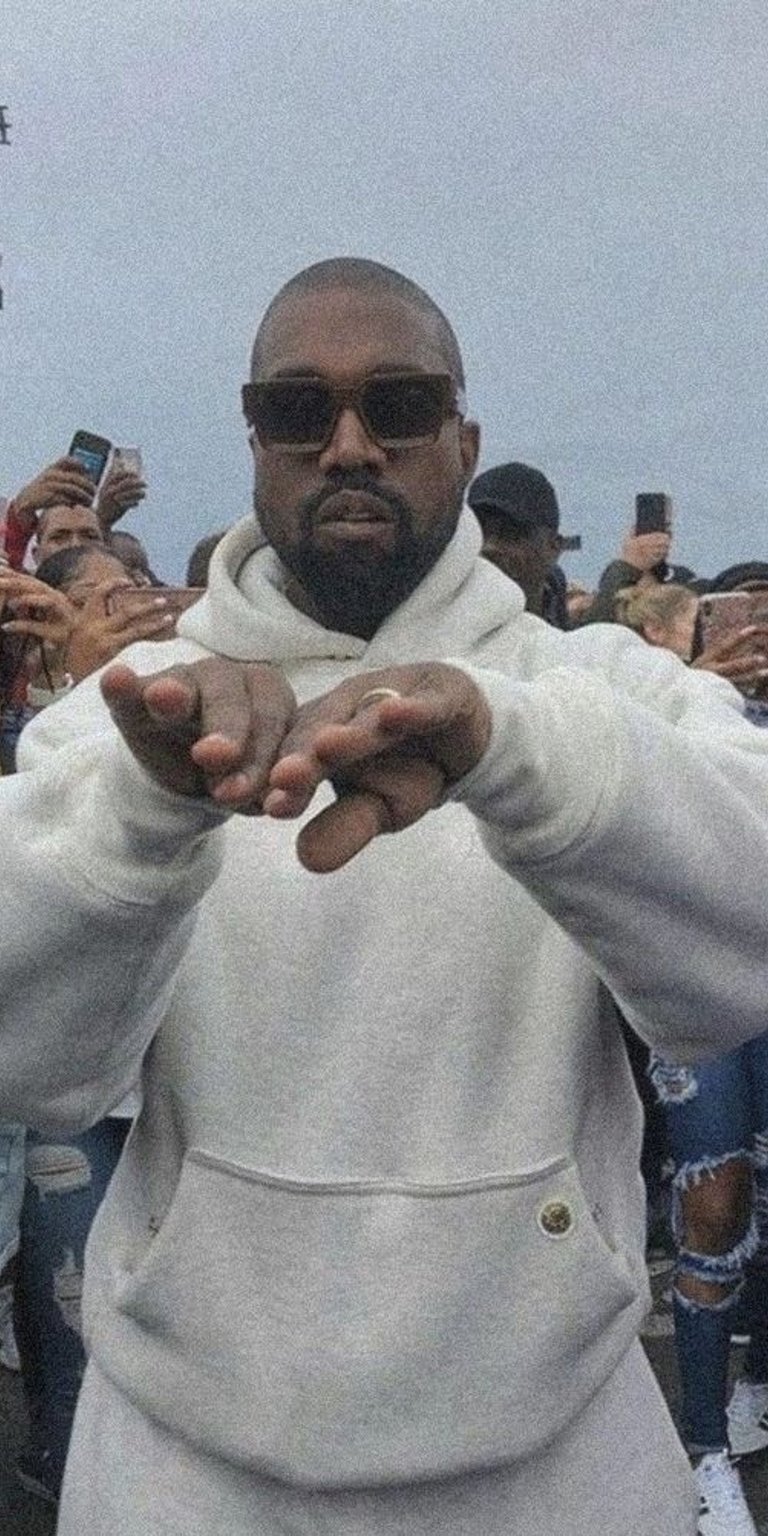 Kanye West wearing white hoodie with a crowd taking picture of him on the back wallpaper