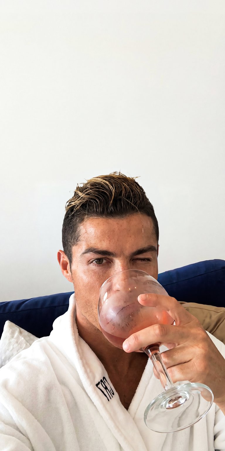 This high-definition wallpaper features global football icon Cristiano Ronaldo (CR7) in a candid, luxury lifestyle setting. Dressed in a premium white spa robe and holding a glass of rosé wine, this image captures the elite relaxation side of the world's most famous athlete. Perfect for fans of Manchester United, Real Madrid, Al Nassr, and Portugal who want a high-class, minimalist aesthetic for their mobile lock screen.