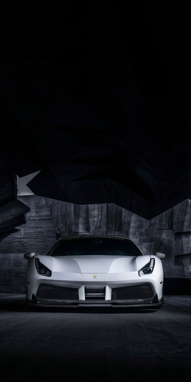 This high-contrast 4K wallpaper features a white Ferrari 488 Pista parked in a dark, architectural concrete garage. Designed as an OLED / AMOLED wallpaper for iPhone, the deep black shadows and sharp lighting highlight the aggressive front-end styling of the supercar.
