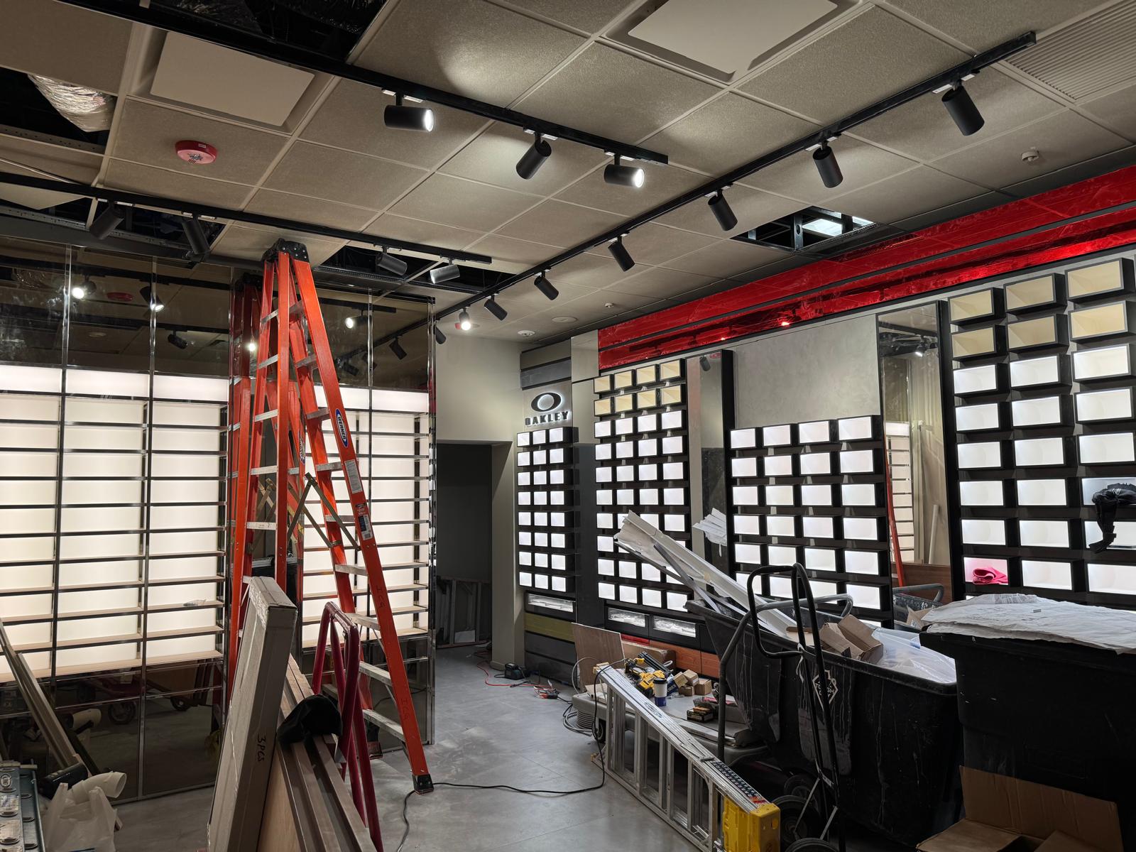 Completed LensCrafters sales floor with backlit frame display walls, Oakley feature wall and black track lighting
