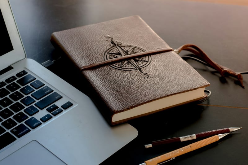 A notebook with a compass enscribed on it, sitting alongside a laptop