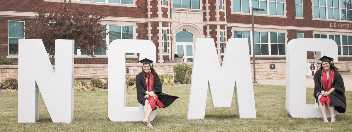 Graduates sitting on letters representing NCMC