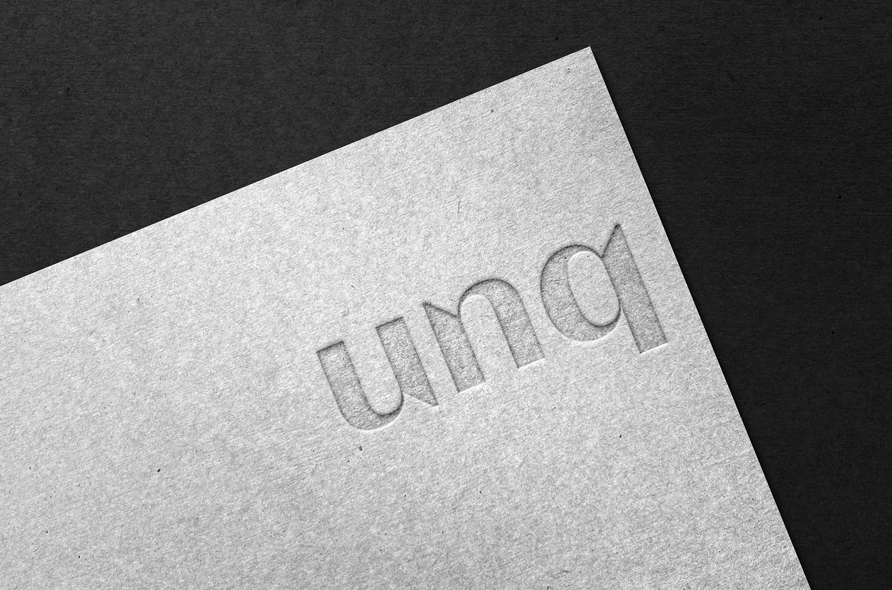 UNQ wordmark embossed on charcoal paper