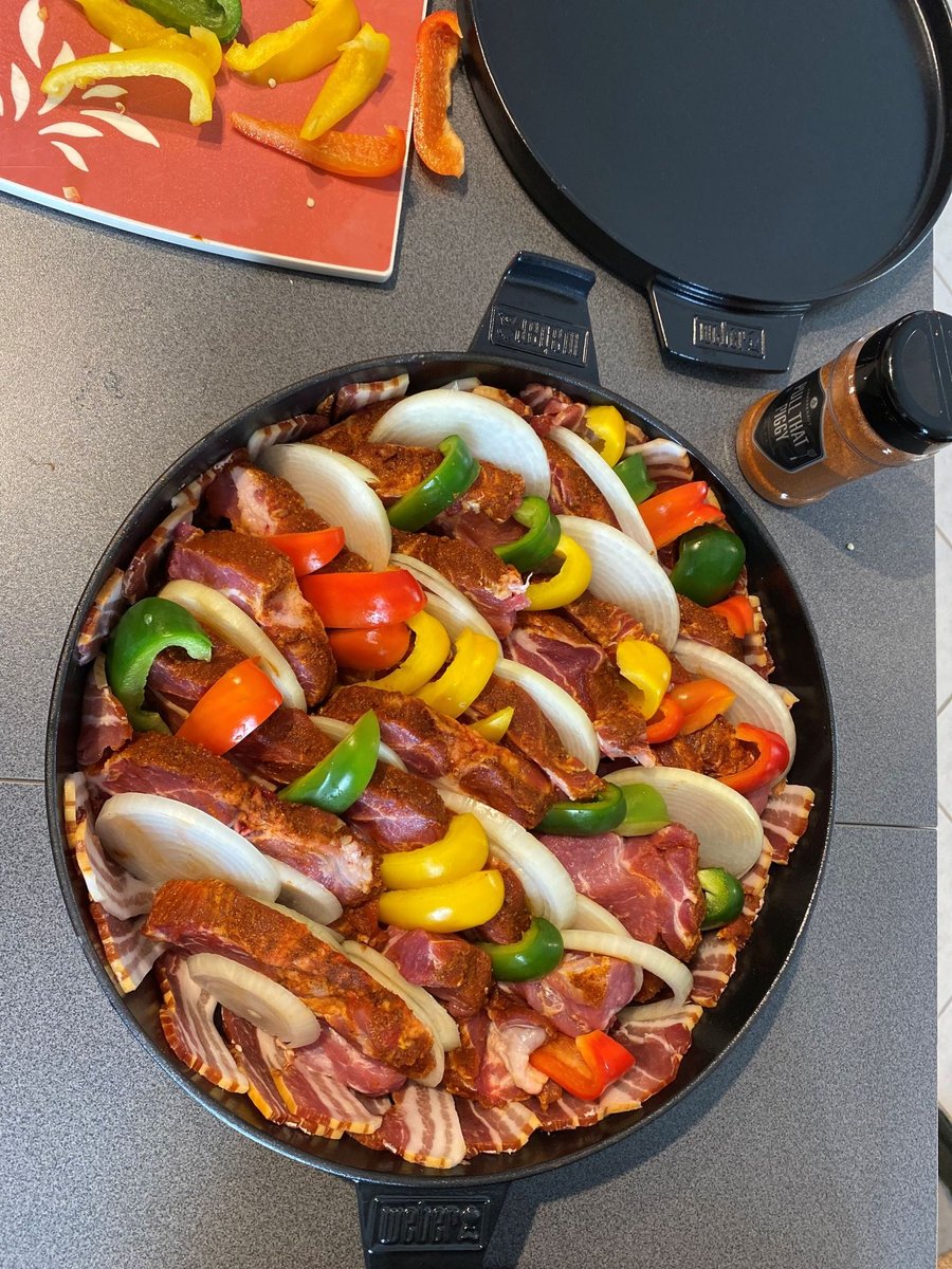 Schichtfleisch roh im Dutch Oven: Fleisch, Zwiebelringe und Paprika in Schichten, von oben fotografiert