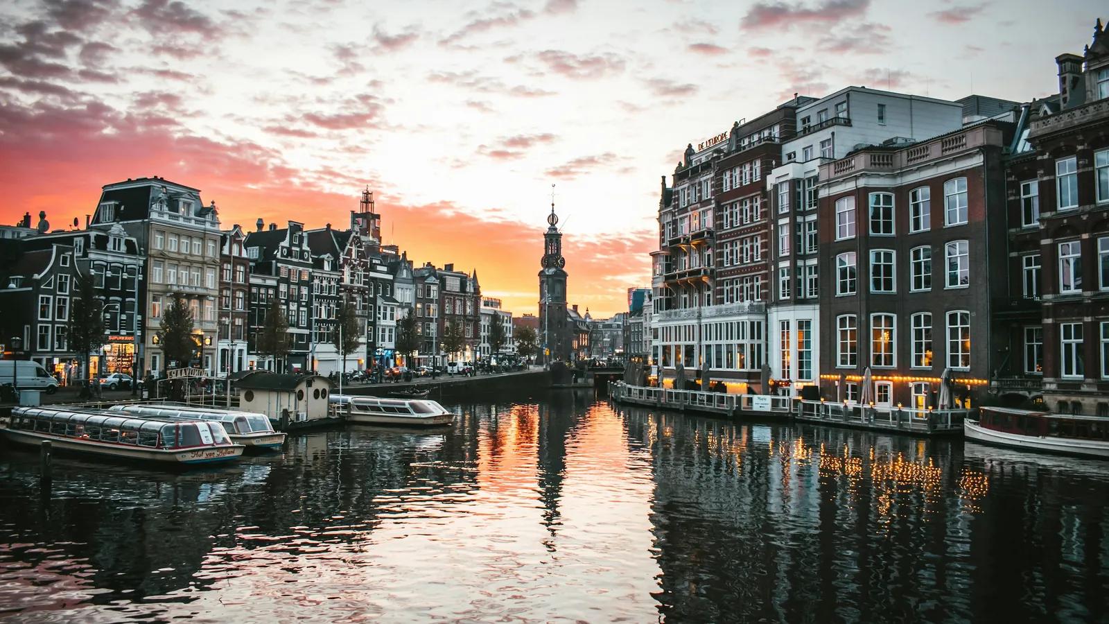 Grachtenboote auf der Amstel bei Sonnenuntergang, dahinter der Munttoren in Amsterdam