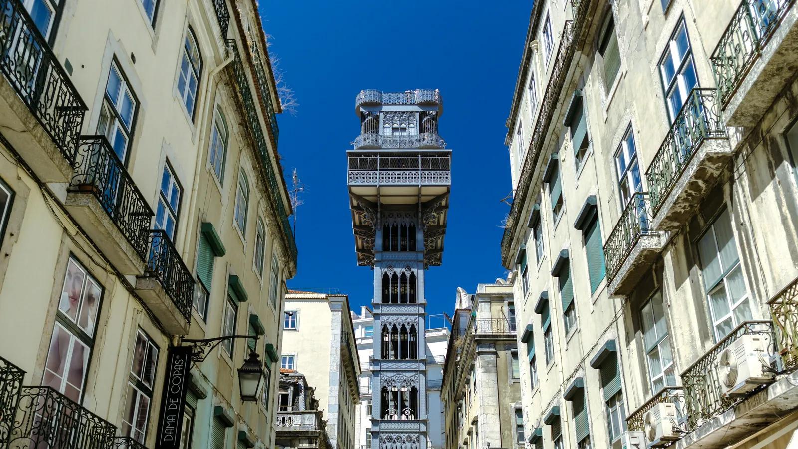 Elevador de Santa Justa entre prédios antigos da Baixa de Lisboa, com céu azul