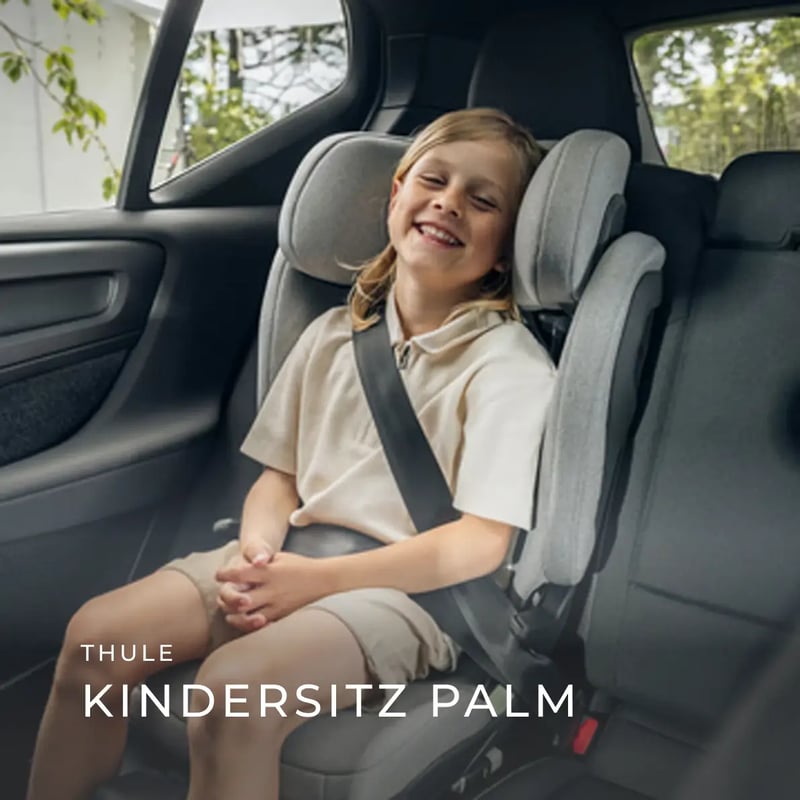 Lachendes Kind sitzt angeschnallt in einem grauen Thule-Kindersitz auf der Rückbank eines Autos