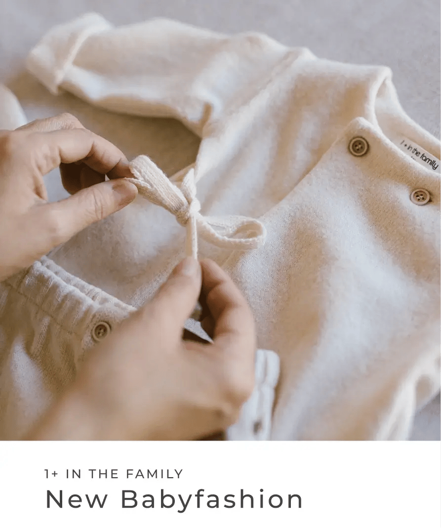 Hände binden eine Schleife an einem hellen Baby-Outfit aus weichem Stoff. 1+ in the family: New Babyfashion.