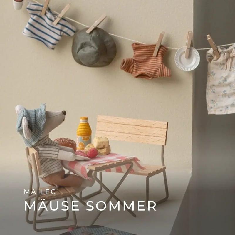 Maileg Stoffmaus sitzt an einem kleinen Tisch mit Picknick, im Hintergrund hängen Miniaturkleidung und Accessoires