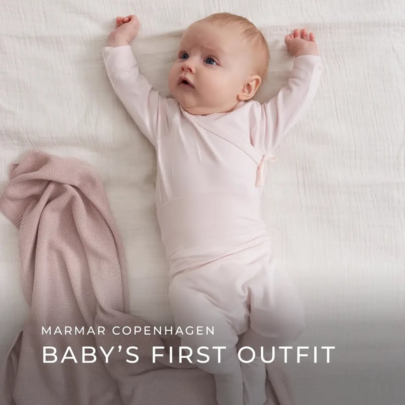 Ein neugeborenes Baby liegt in einem hellrosa Wickel-Outfit aus der „Baby’s First Outfit“ Serie von MarMar Copenhagen