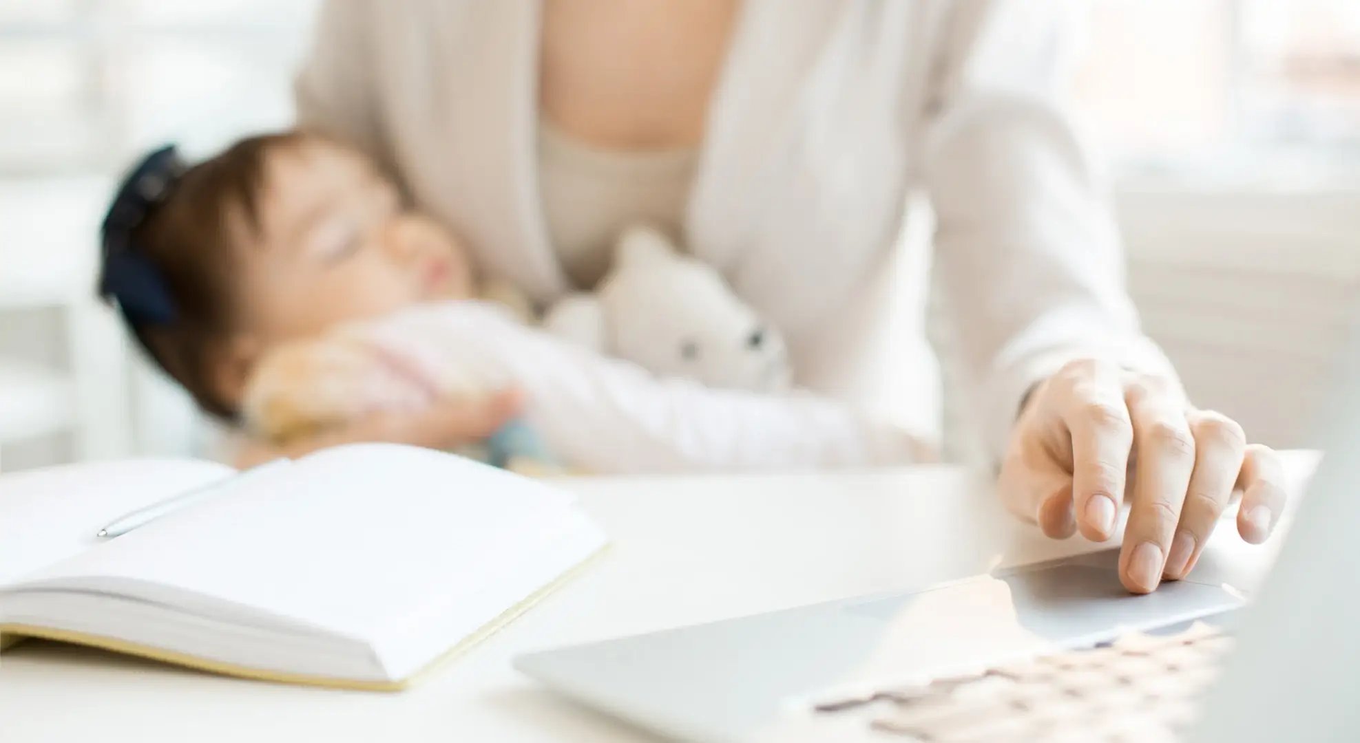 eine Mutter mit Baby auf dem Arm tipp auf einem Laptop etwas ein