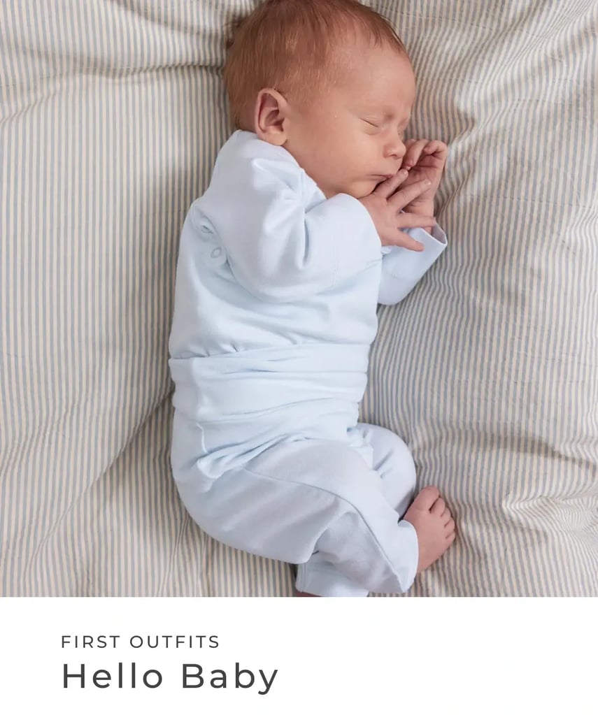 Schlafendes Neugeborenes in einem hellblauen Erstlings-Outfit auf gestreifter Bettwäsche. First Outfits – Hello Baby.