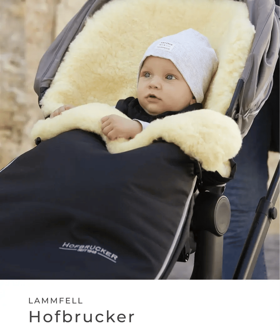 Ein Baby liegt in einem Kinderwagen auf einem weichen Lammfell und ist mit einem Hofbrucker Fußsack zugedeckt. Lammfell: Hofbrucker.