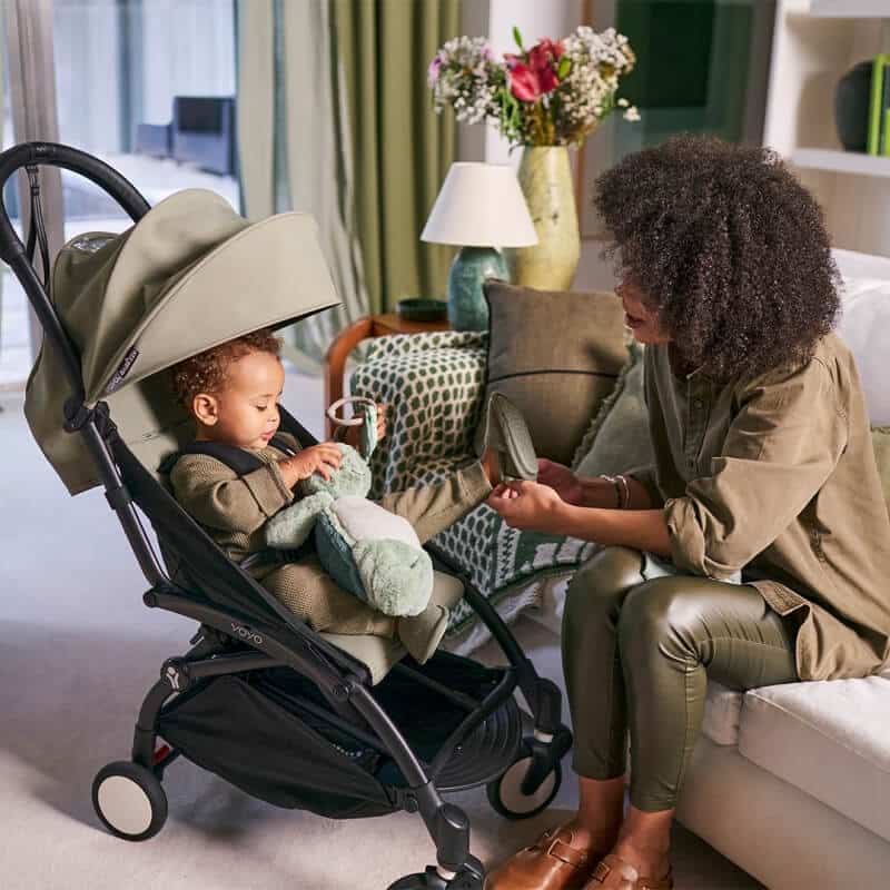 Mutter sitzt auf einem Sofa, ihr Kind im Babyzen YOYO vor ihr