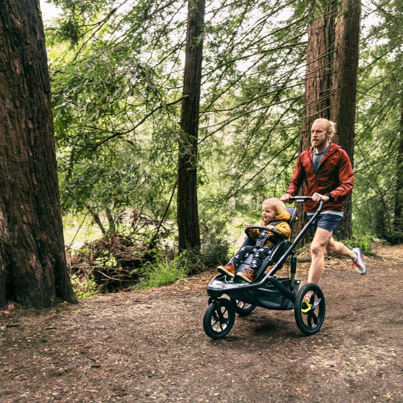Vater joggt mit seinem Kind im Veer Switchback durch den Wald