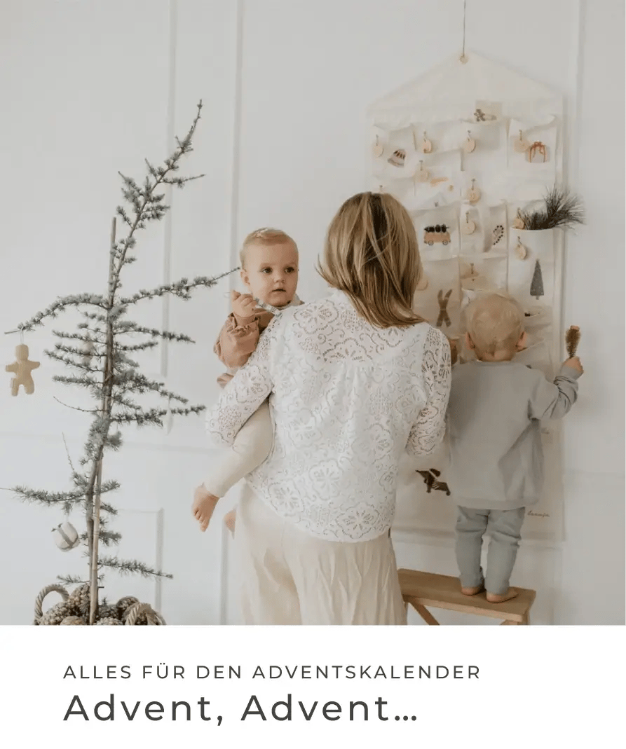 Mutter steht mit zwei kleinen Kindern vor einem hellen Adventskalender neben einem geschmückten Weihnachtsbaum. Alles für den Adventskalender: Advent, Advent...