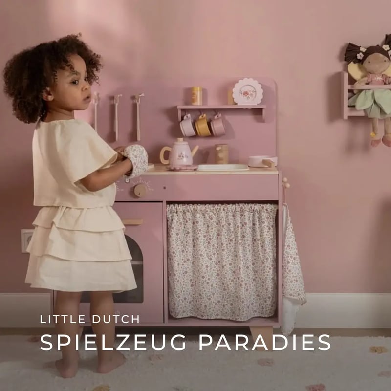 ein kleines Mädchen steht vor einer roasafarbenen Spielküche