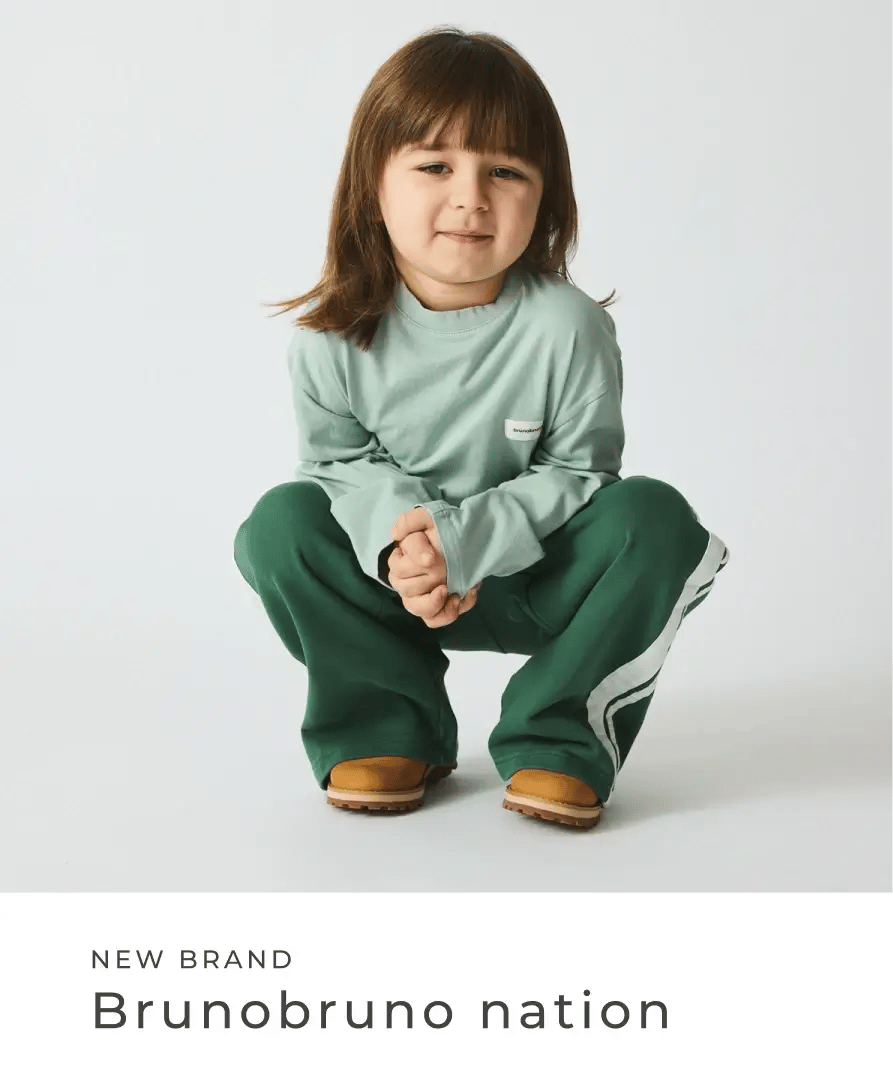 Kind sitzt in grüner Hose und mintfarbenem Oberteil vor hellem Hintergrund. New Brand: Brunobrunonation.