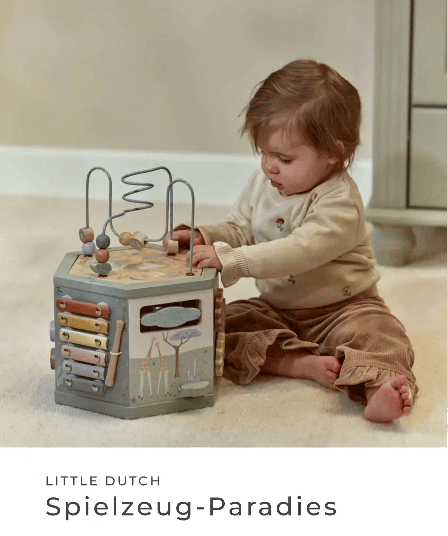 Kleinkind sitzt auf dem Boden und spielt mit einem Motorikwürfel aus Holz. Little Dutch: Spielzeug-Paradies.