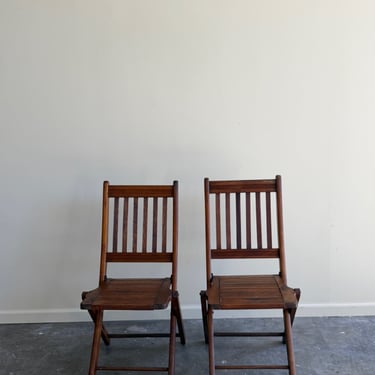 Stained pine folding chairs. Sold as a pair.