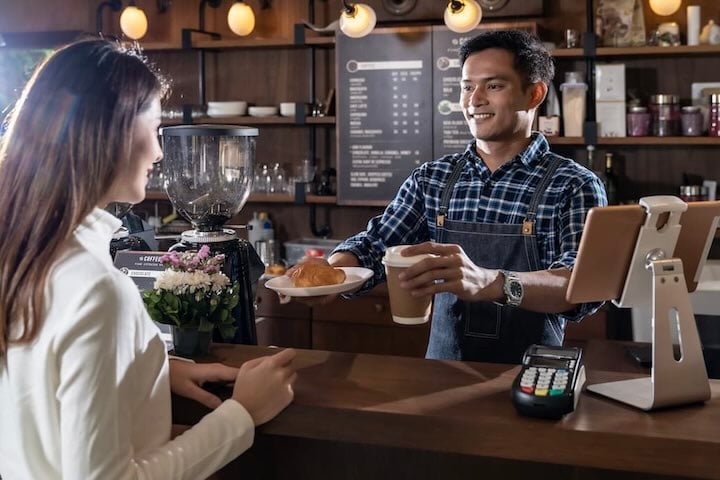 A barista serving a coffee and pastry to a customer at a café counter