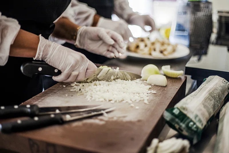 Food handler in disposable gloves chopping vegetables on a board in a commercial kitchen