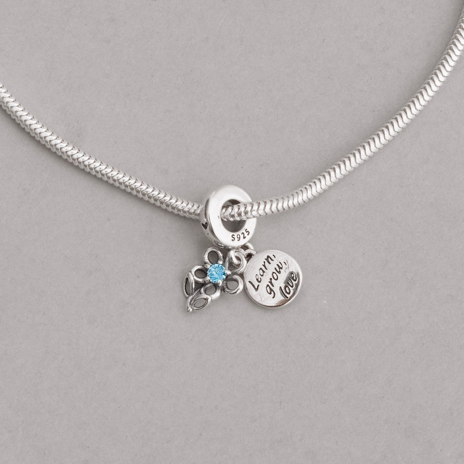 Berloque pingentes flor com zircônia azul e placa learn, grow, love envelhecido