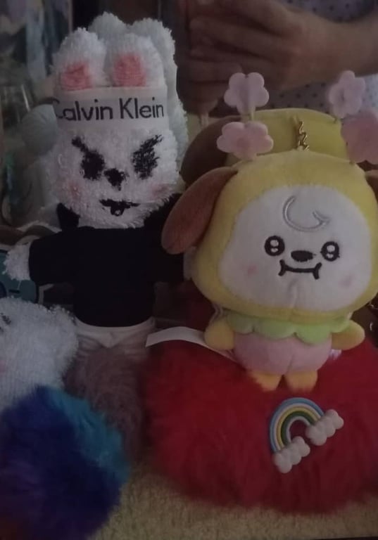 Dos peluches: uno blanco con diadema y otro amarillo con flores, sobre base roja con arcoíris
