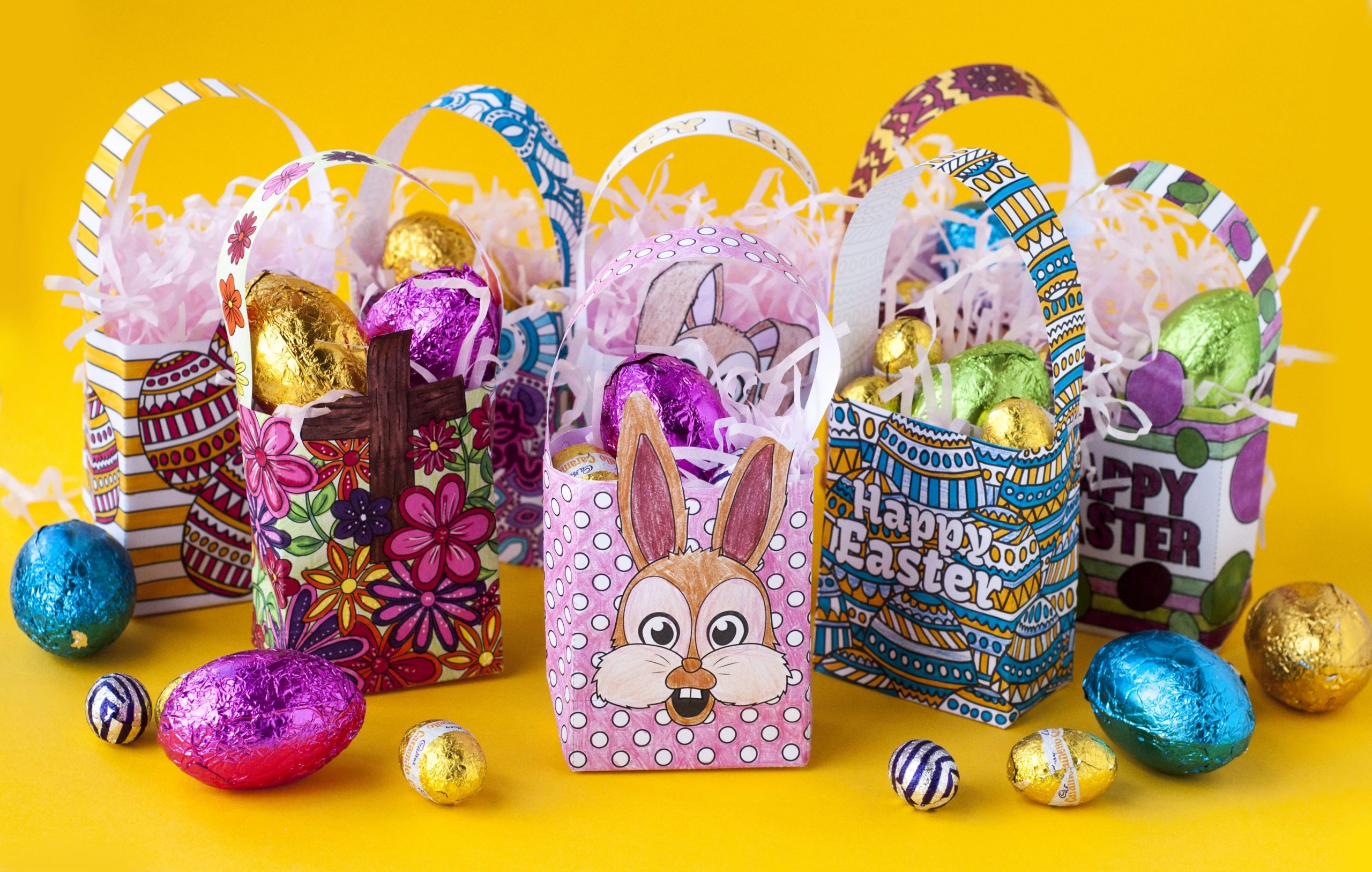 A collection of 8 Do it Yourself paper easter baskets with chocolate easter eggs scattered around in the foreground of the image