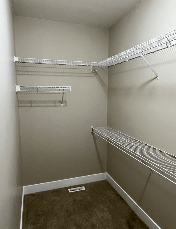 Freshly painted walk-in closet with an even beige finish on the walls, white shelving, and clean white baseboards
