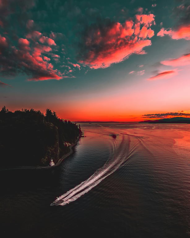Boat leaving a wake in calm waters at sunset, with a vibrant sky and silhouetted trees along the shore