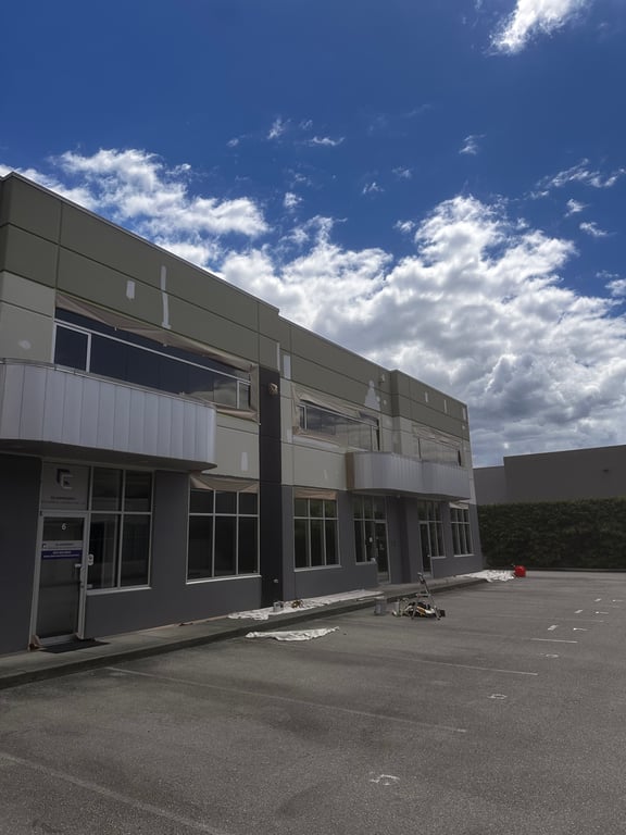 Two-storey commercial building repainted in grey and charcoal, with clean cut lines around the windows, canopies, and entry doors