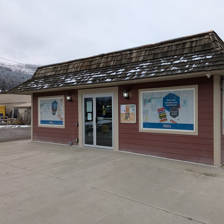 Exterior of a red pharmacy building with two large windows featuring posters about medication management and a glass entrance door on a snowy day