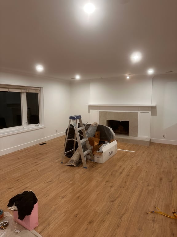 Finished living room with even white walls and ceiling, a white fireplace mantel and surround, and pot lights throughout