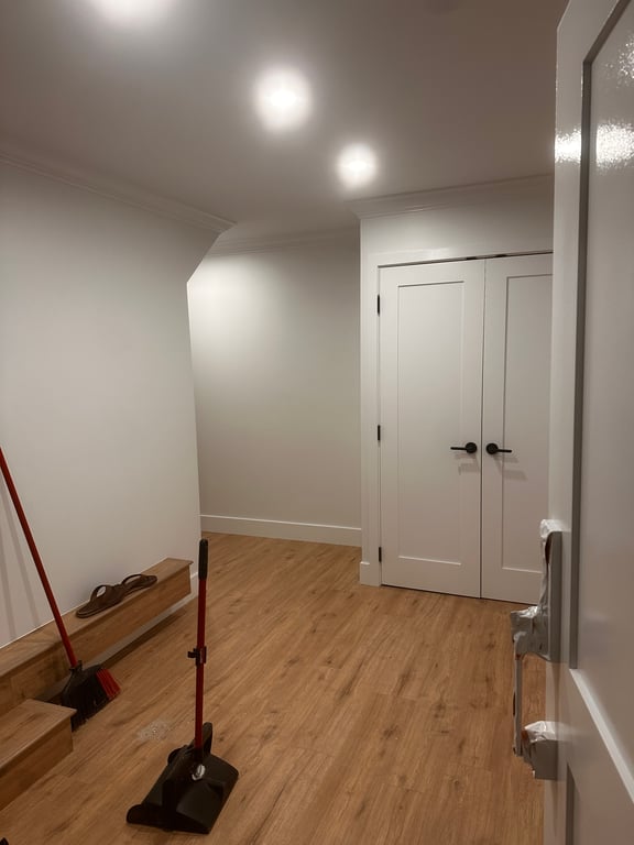 Freshly painted hallway with white walls, crown moulding, and sprayed white double closet doors with black hardware