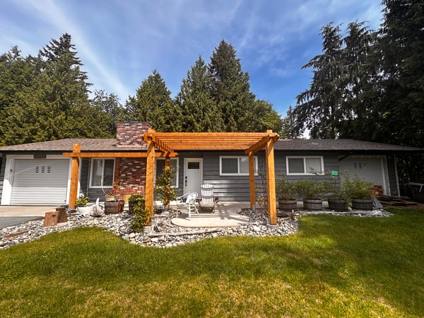 Repainted single-storey house with grey siding, crisp white trim, a white front door and garage door, and a cedar pergola over the front patio.
