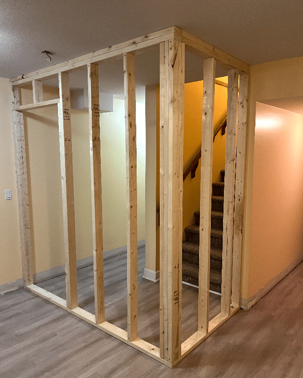 Unfinished wooden wall framing forming a small enclosed structure around a staircase opening inside a basement or interior room