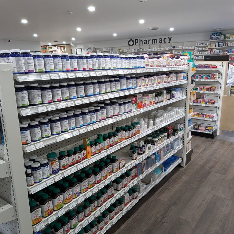 Pharmacy shelves stocked with vitamins, supplements, and health products in organized rows, with additional pharmacy shelves in the background