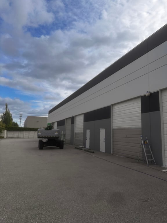 Row of commercial warehouse units finished in a two-tone white and grey exterior scheme, including the overhead doors and man doors