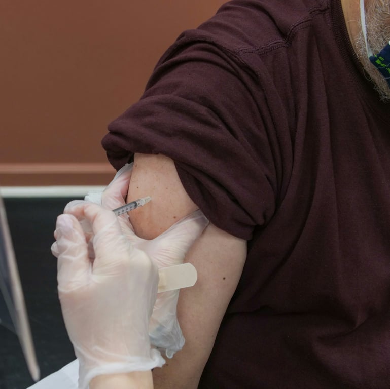 Healthcare professional administering a vaccination into a patient's upper arm, with gloves and a syringe visible.