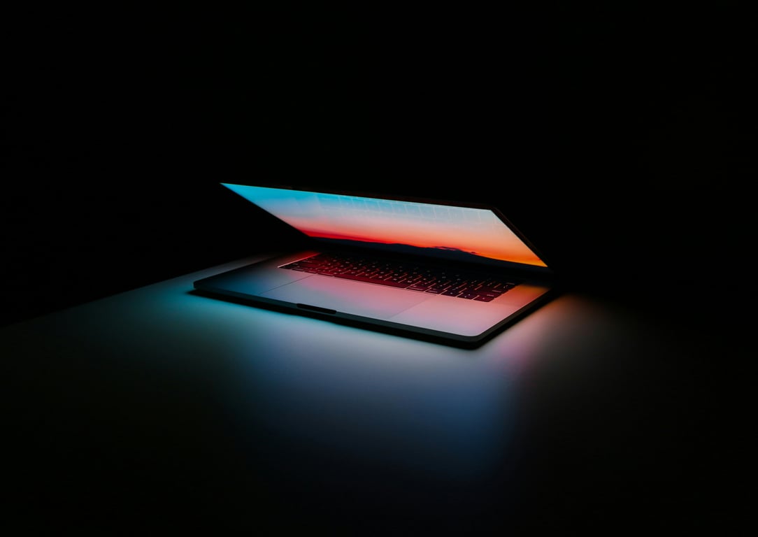Laptop partially closed with a colorful screen glowing in a dark environment.